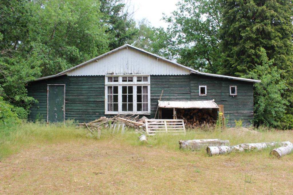 De achterkant van de barak in woonoord Baarschot. Boven de kozijnen zijn de gaten in het hout duidelijk te zien, maar ook op ander plekken kun je tussen de planken gaten zien.